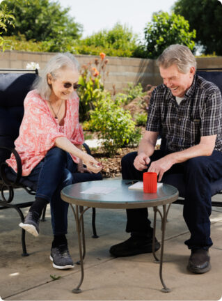 woman with sunglasses sitting next to a man with grey hair putting something on the table