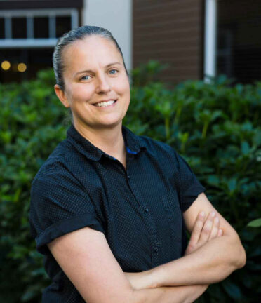 a woman smiling with a black shirt and her hair in a bun