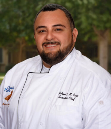 smiling man with short dark hair and a beard in a white chefs coat