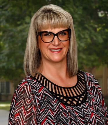 smiling woman with shoulder length hair and bangs wearing glasses