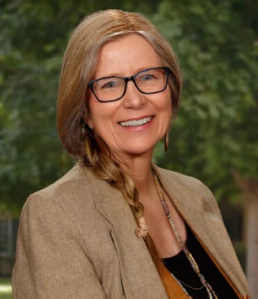 smiling woman with glasses and a side braid wearing a blazer