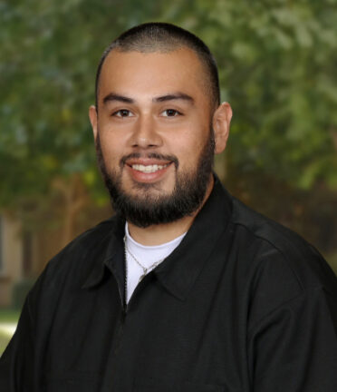 smiling man with a beard and very short hair wearing a black shirt with a white t-shirt underneath